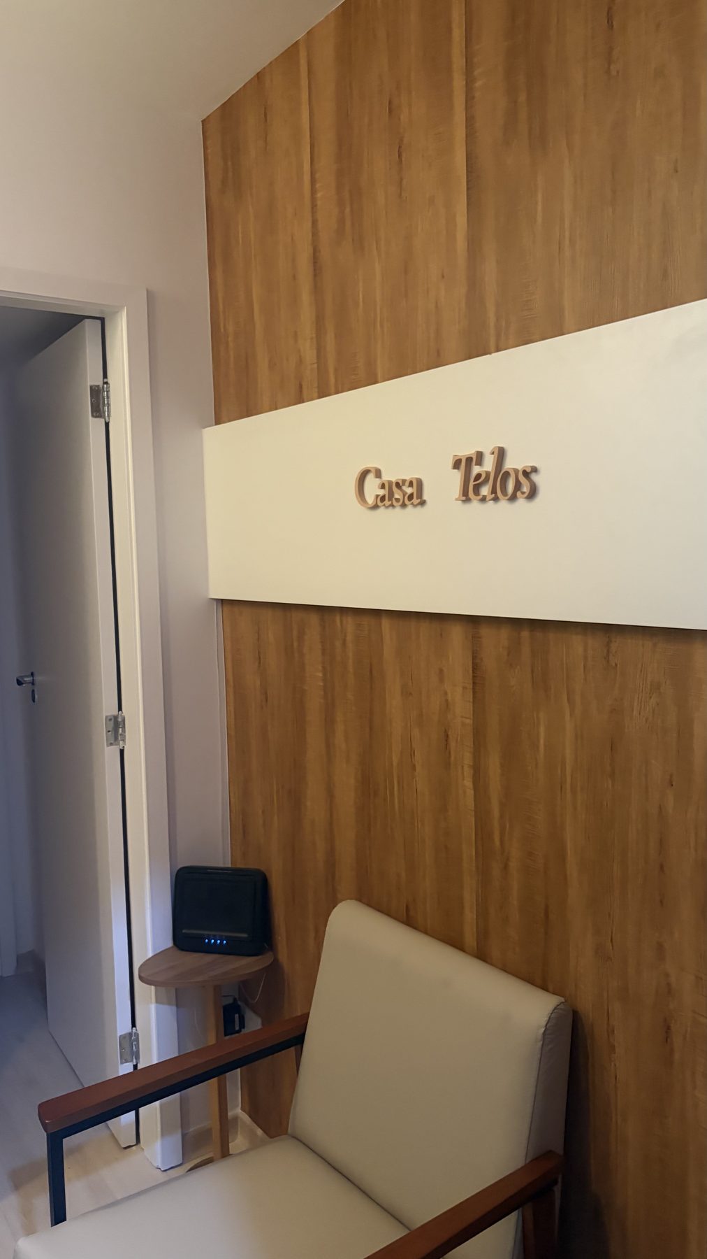 Recepção da Casa Telos com poltrona e letreiro na parede de madeira ripada