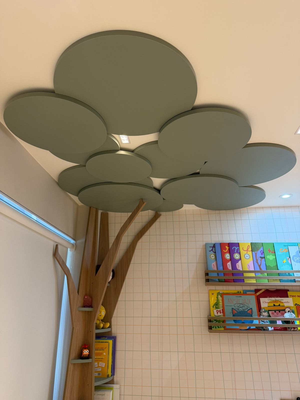 Árvore de marcenaria com copa em painéis verdes no teto da sala infantil